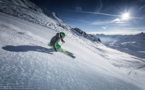 Ein Skifahrer saust die frisch präparierte Piste mit Bergpanorama und Sonnenschein im Hintergrund hinunter
