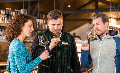 Zwei Personen und ein Sommelier stehen in der Vinnova mit einem vollen Weinglas in der Hand und riechen daran