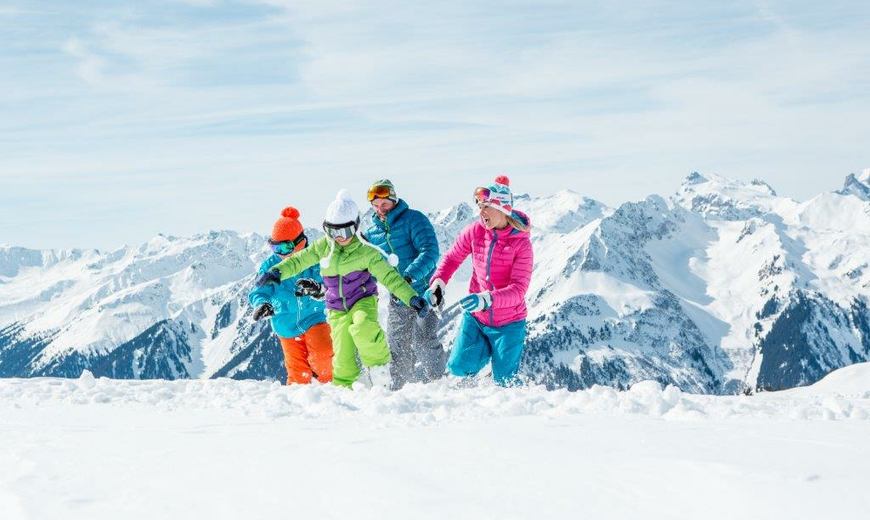 Eine Familie mit zwei Kinder und Skikleidung rennt durch den Schnee
