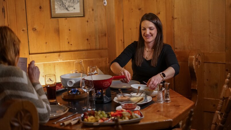 Zwei Personen sitzen in einer gemütlichen Stube am gedeckten Tisch mit Käsefondue. | © Vanessa Strauch - Silvretta Montafon
