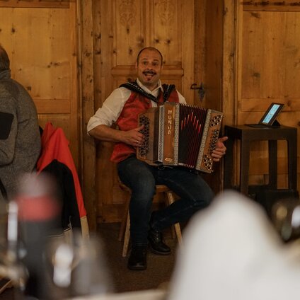 Ein Musiker musiziert und singt mit einer Ziehharmonika in einer gemütlichen Berghütte im Skiegbiet Silvretta Monatfon. | © Vanessa Strauch - Silvretta Montafon