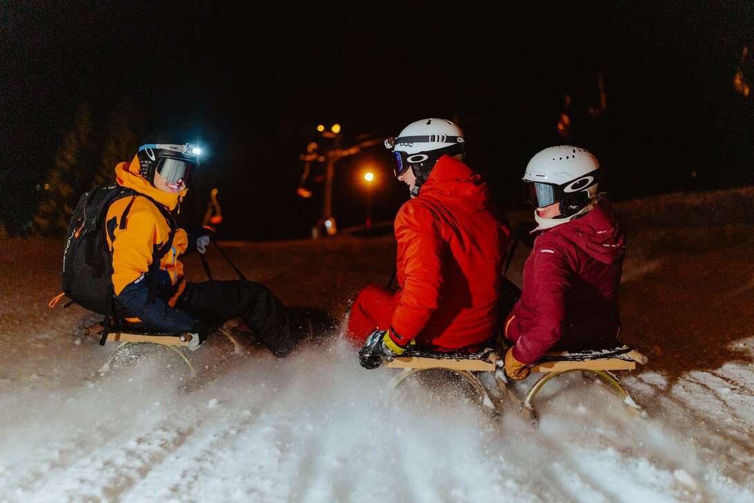 Drei Personen in Skikliedung rodeln auf einem Schlitten am Abend. | © Silvretta Montafon - Marie Schilcher