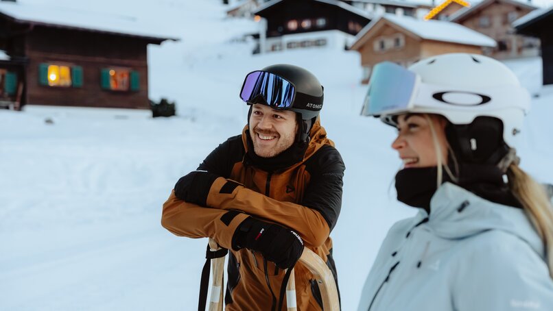 Zwei lächelnde Personen in Skikleidung mit Helm und Skibrille, der Mann lehnt auf einem Rodel. | © Silvretta Montafon - Marie Schilcher