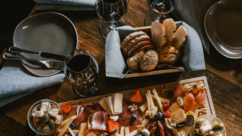 Ein Tisch mit Käsebrett, Botkorb und Rotwein. | © Silvretta Montafon - Vanessa Strauch