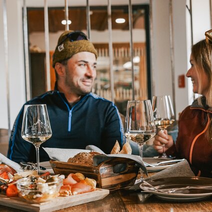 Drei Personen an einem Tisch mit Käse, Brot und Wein. | © Silvretta Montafon - Vanessa Strauch