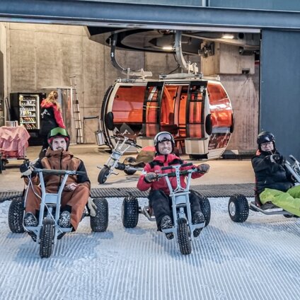 Drei Männer sitzen beim Ausstieg einer Gondel auf einem Mountain Cart im Schnee. | © Silvretta Montafon