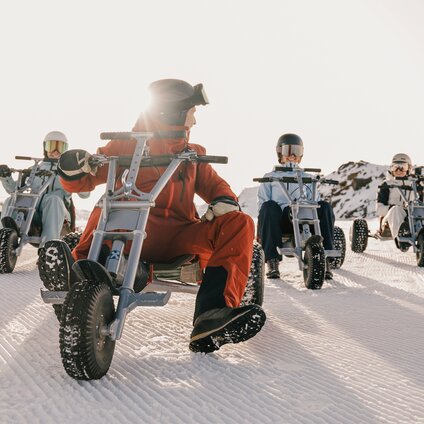 Fünf Personen auf einem Mountaincart auf einer Skipiste am Morgen bei Sonnenaufgang. | © Silvretta Montafon - Niklas Kirchler