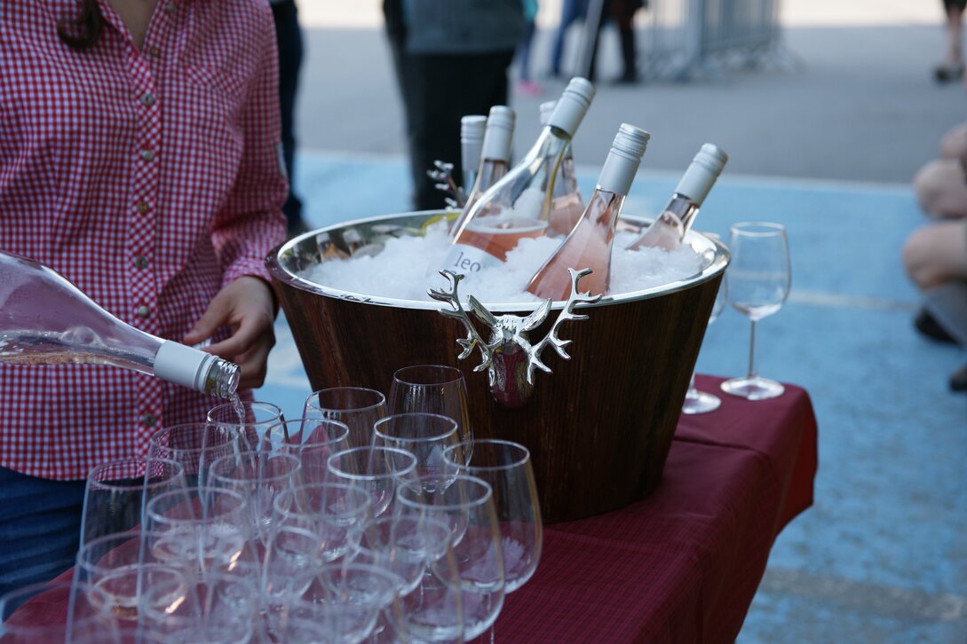Weinflaschen in einem Weinkühler und aufgestellt Weingläser, welche gerade gefüllt werden | © Silvretta Montafon - Ruth Barthold