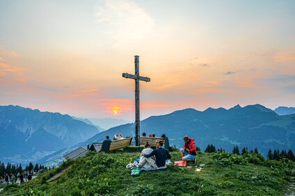 Viele Personen stehen am Gipfelkreuz und genießen den Sonnenuntergang bei der Sonnwendfeier in der Silvretta Montafon. | © Silvretta Montafon - Vanessa Strauch