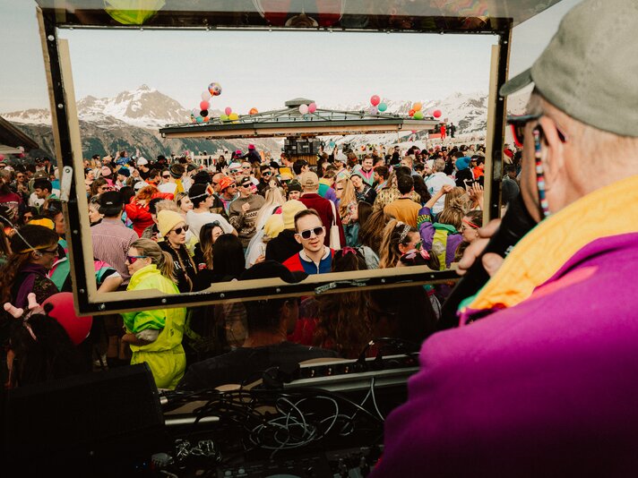 Eine Menschenmenge mit vielen feiernen Menschen in bunter 80er Jahre Kleidung und DJ im Vordergrund. | © Silvretta Montafon - by goodguypaez