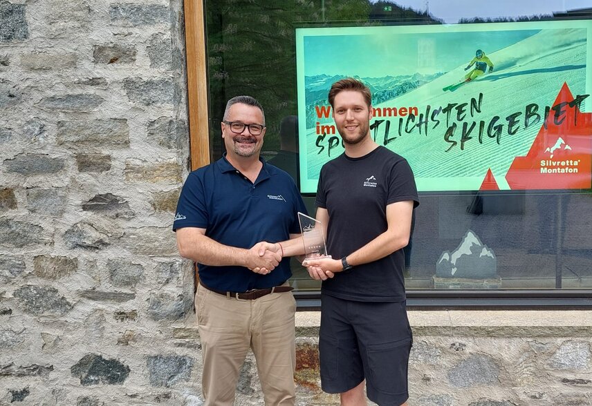 Zwei Männer überreichen sich einen Award zum umweltschonenden Skigebiet vor der Alpin Sport Zentrale in Schruns | © Silvretta Montafon