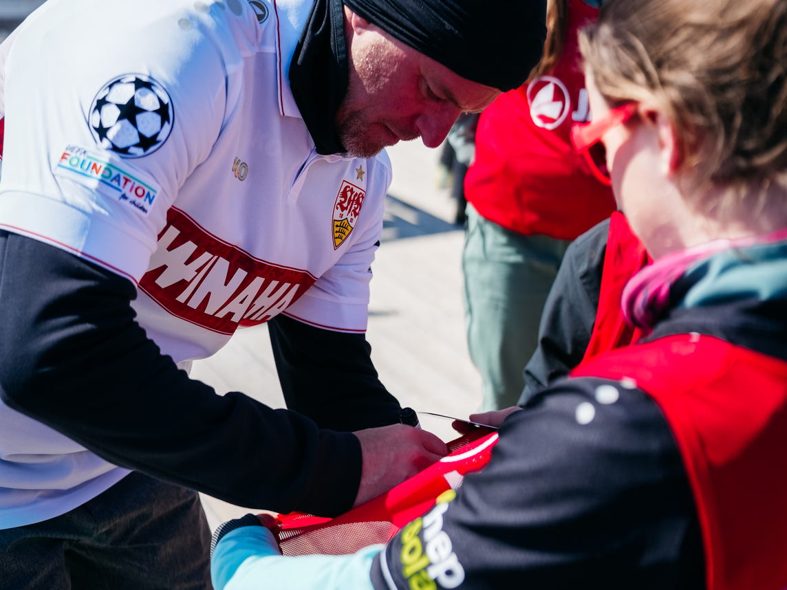 Eine Fußballlegende vom VfB Stuttgart unterschreibt ein Trikot für einen kleinen Fan | © VfB Stuttgart - Silvretta Montafon