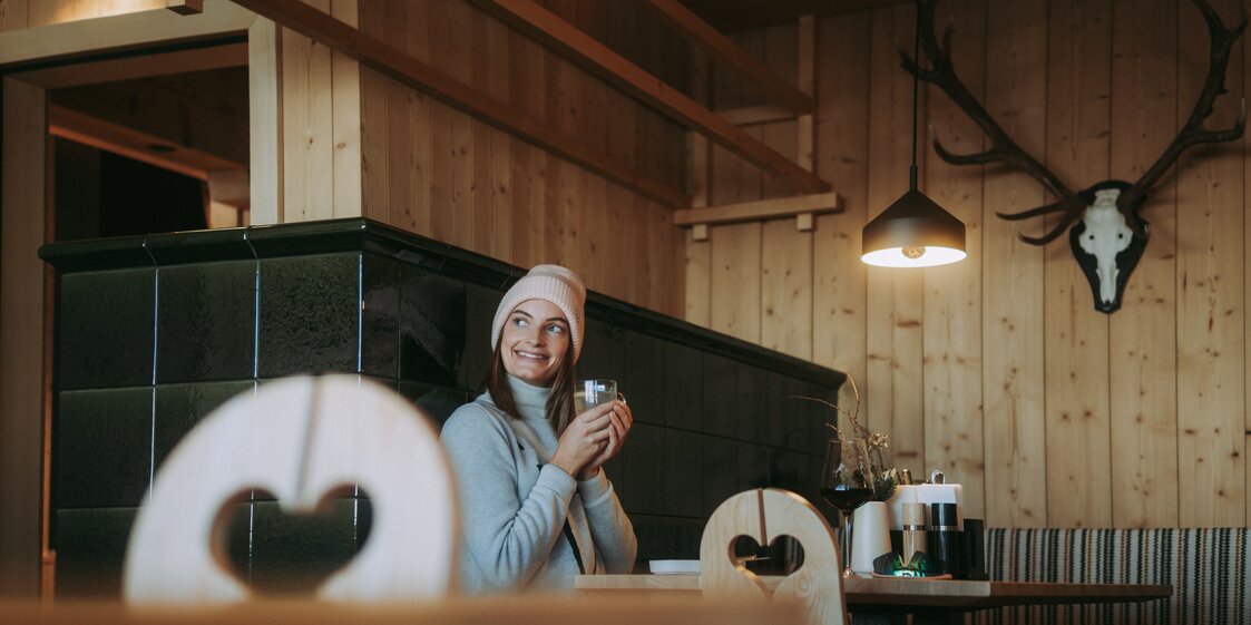 Eine Frau wärmt sich an einem Kamin mit einem Kaffee in der Hand. | © Silvretta Montafon - WanderlustAllgäu