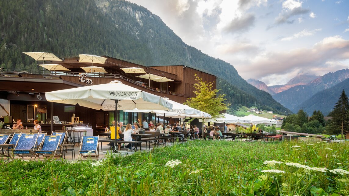  Ansicht des Restaurants von Aussen mit grüner Wiese im Vordergrund, Terrasse, Liegestühlen und Sonnenschirmen | © Silvretta Montafon - Stefan Kothner