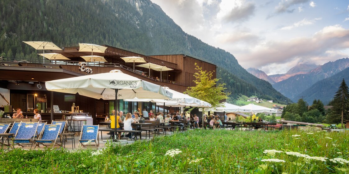  Ansicht des Restaurants von Aussen mit grüner Wiese im Vordergrund, Terrasse, Liegestühlen und Sonnenschirmen | © Silvretta Montafon - Stefan Kothner