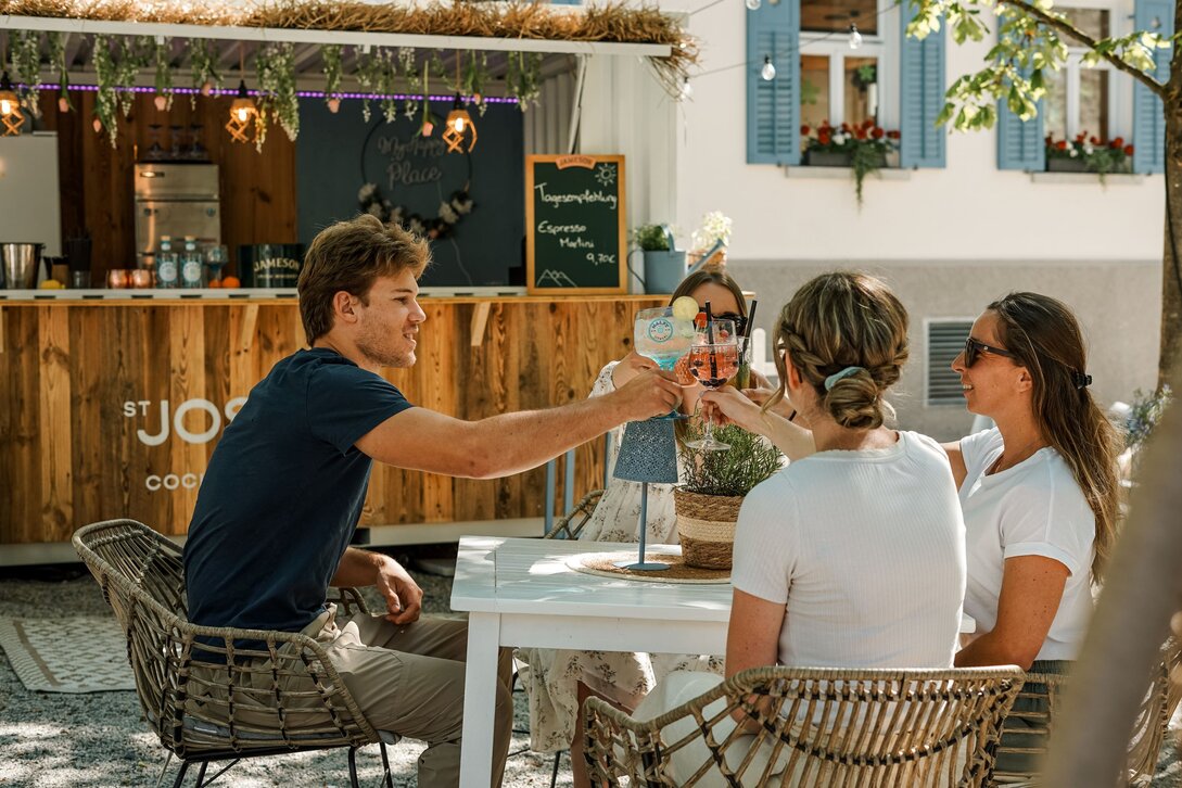 Drei Frauen und ein Mann stoßen mit ihren Getränken in St. Josefs Cocktailgarten an. | © Silvretta Montafon - Vanessa Strauch