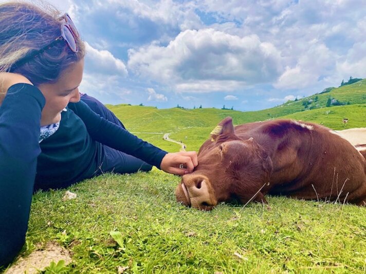 Luisa Idler in den Bergen | © Luisa Idler - Silvretta Montafon Ein Mädchen liegt auf einer Wiese in den Bergen und streichelt ein Kälbchen. | © Luisa Idler - Silvretta Montafon