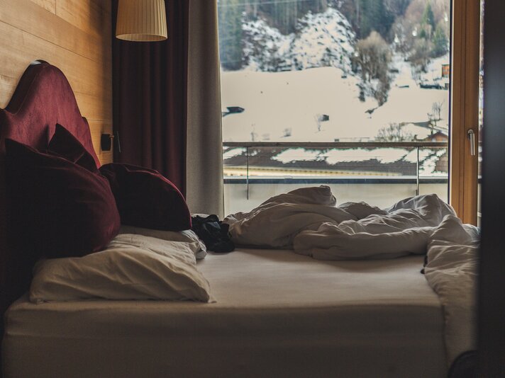 Eine Bett mit Fenster und Aussicht in die verschneite Landschaft. | © Silvretta Montafon - Roadtyping