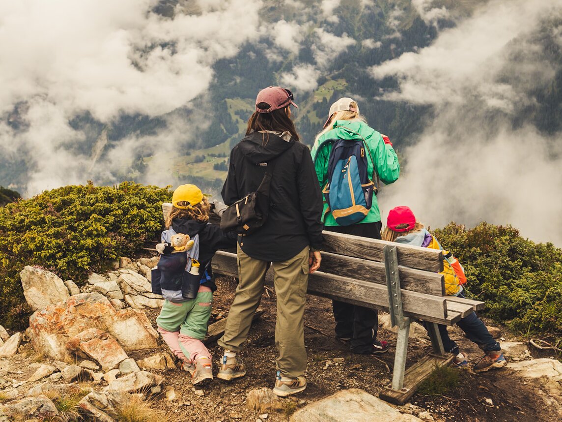 Aussicht genießen - Silvretta Montafon | © Silvretta Montafon - Roadtyping Zwei Erwachsene und zwei Kinder pausieren bei einer Bank in den Bergen und genießen die Aussicht. | © Silvretta Montafon - Roadtyping