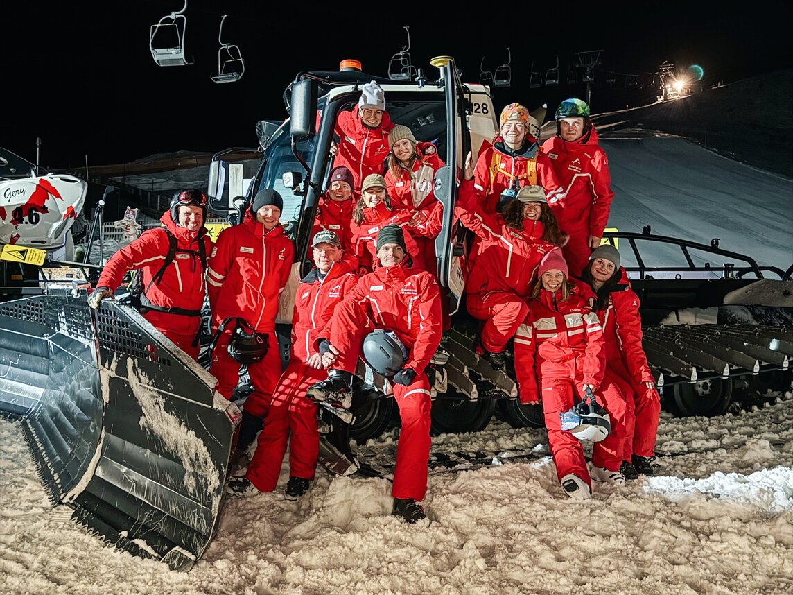 Eine Gruppenfoto mit 6 Skilehrern in roter Uniform am Abend vor einem Pistenbully in der Silvretta Montafon. | © Viola Schwigon - Silvretta Montafon