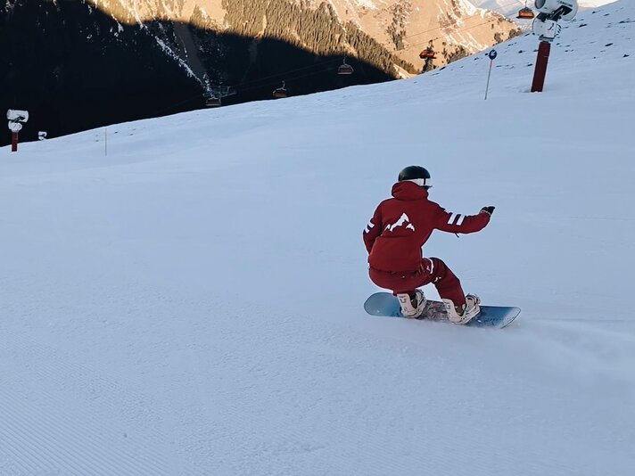 Eine Snowboardlehrerin fährt die Piste in roter Unifrom hinunter. | © Viola Schwigon - Silvretta Montafon