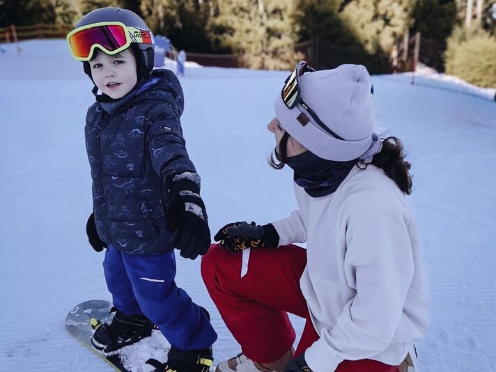 Ein Junge auf einem Snowboard und seine Snowboardlehrerin kniet neben ihm.  | © Viola Schwigon - Silvretta Montafon