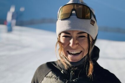 Eine Nahaufnahme mit einer lachenden Skilehrerin mit Mütze, Sonnenbrille, schwarzer Jacke und roter Skihose. | © Viola Schwigon - Silvretta Montafon