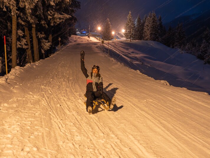 Eine Frau auf einem Rodel am Abend in der Silvretta Montafon. | © Silvretta Montafon - Lisa von Abenteuermomente