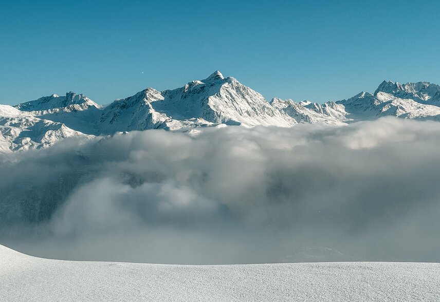 Verschneites Bergpanorama mit blauem Himmel und Nebel im Tal. | © Silvretta Montafon - Vanessa Strauch