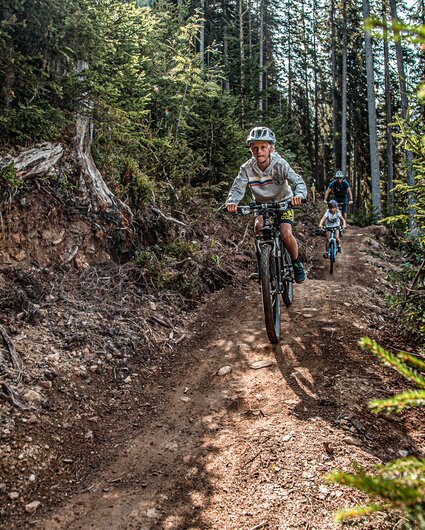 Eine Junge im Vordergrund und zwei Personen im Hintergund fahren durch den Wald im Bikepark am Hochjoch in der Silvretta Montafon.  | © Silvretta Montafon - Friederike Weber