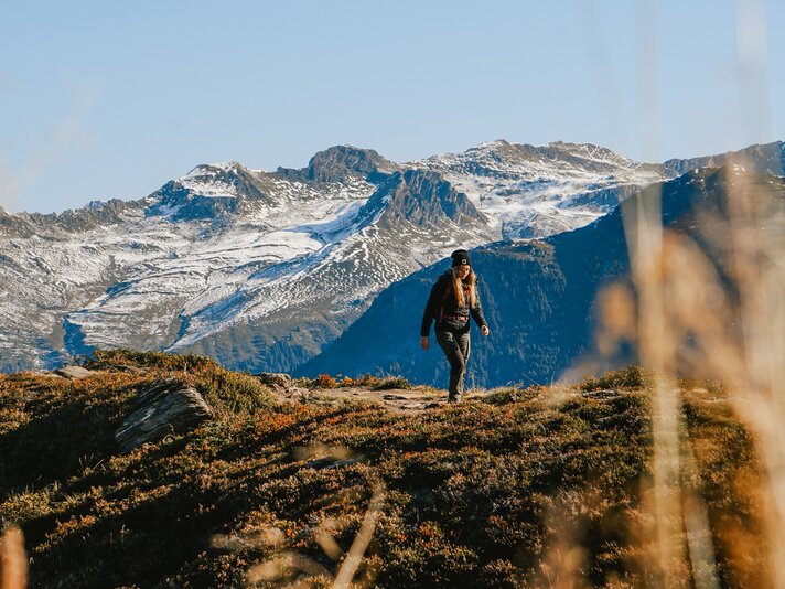 Herbstwanderung Gantakopf - Silvretta Montafon | © Silvretta Montafon - Vanessa Strauch Eine Frau wandert im Herbst mit schneebedeckten Bergspitzen im Hintergrund in der Silvretta Montafon | © Silvretta Montafon - Vanessa Strauch