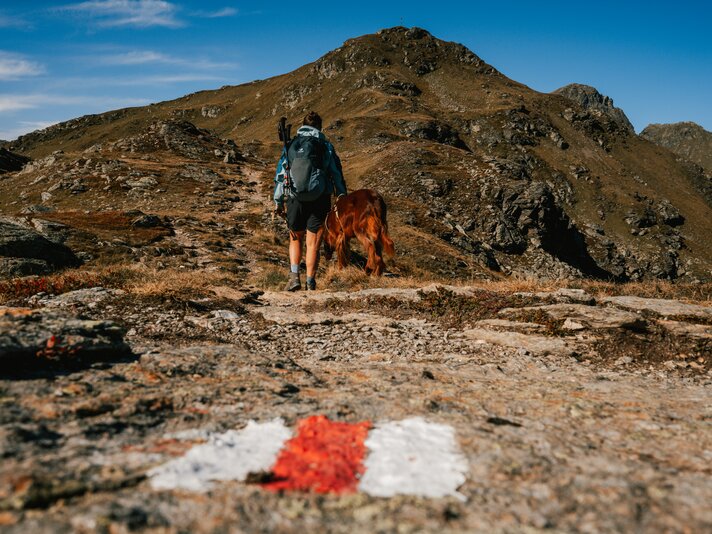 Wanderweg - Silvretta Montafon | © Silvretta Montafon - Vanessa Strauch Die Wanderwegmarkierung mit Wanderin und Hund im Hintergrund. | © Silvretta Montafon - Vanessa Strauch