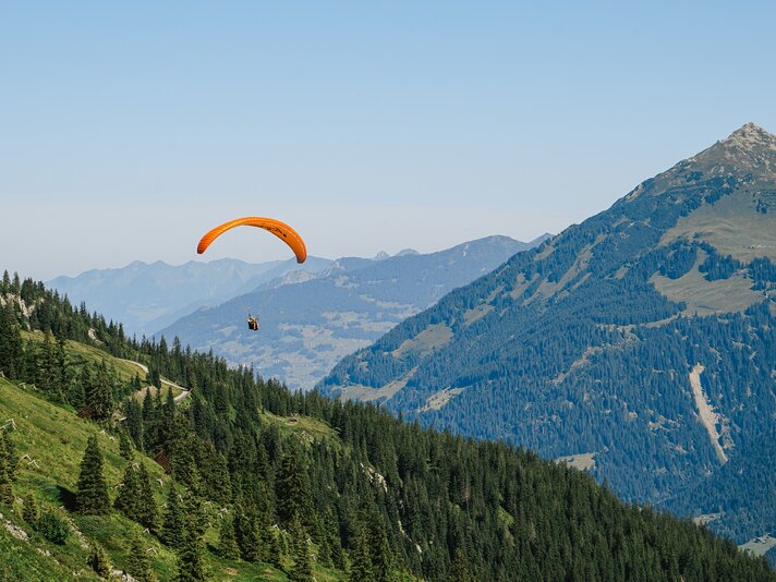 Ein Paraglider fliegt über die Berge eentlang des Wanderweges Lifinar in der Silvretta Montafon. | © Silvretta Montafon - Vanessa Strauch