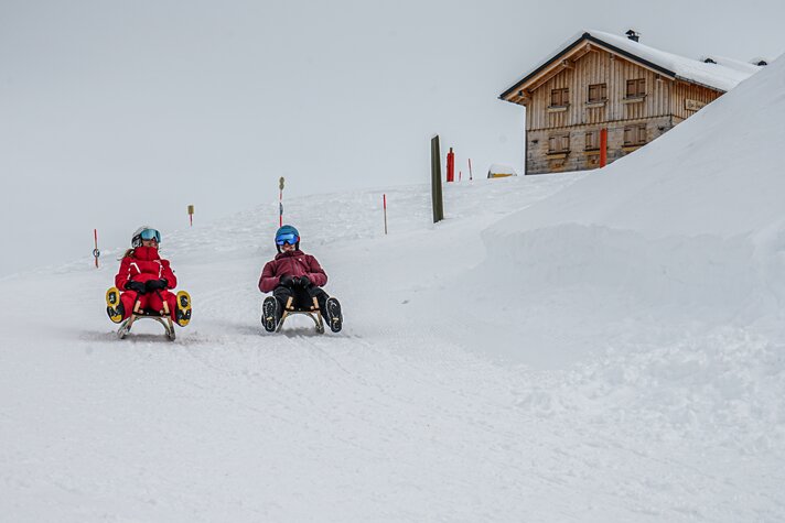 Zwei Freunde lachen beim Rodeln auf der Naturrodelbahn Kapell in der Silvretta Montafon | ©  Silvretta Montafon - Vanessa Strauch