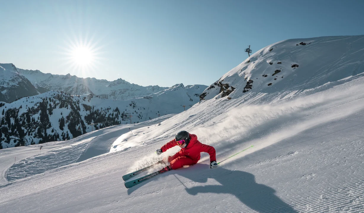 Ein sehr sportlicher Skifahrer in knallig rotem Skianzug carvt die Panorama-Piste in tiefer Hocke bei Sonnenschein hinunter. | © Silvretta Montafon - Jacobo Bonacorsi