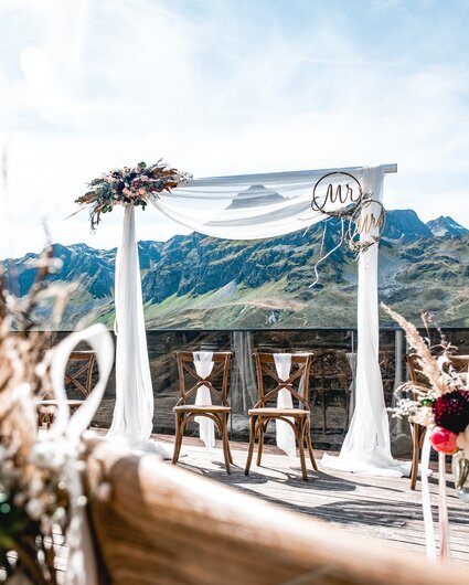 Dekorierter Traubogen und Bestuhlung für eine Hochzeit auf der Terrasse der VINNOVA mit Berge im Hintergrund | © Silvretta Montafon - Patrick Säly