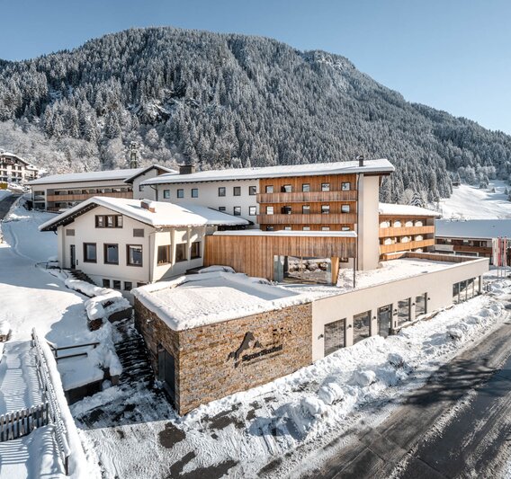 Das Sporthotel Silvretta Montafon schneebedeckt im Vordergrund mit weißen Bergen im Hintergrund | © Silvretta Montafon - blateral