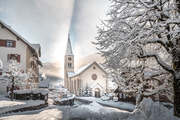 Die Kirche im Ortskern von Gaschurn im Winter mit Berge im Hintergrund | © Silvretta Montafon - blateral