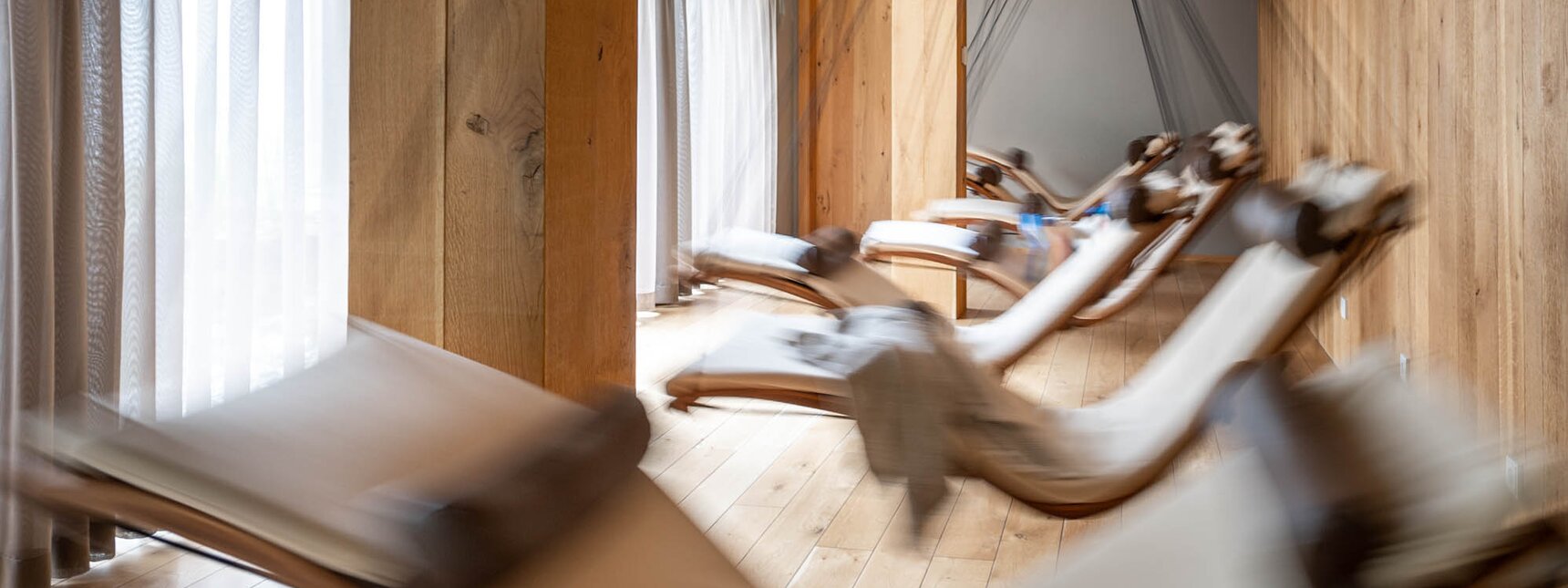 Bewegende Schwebeliegen mit einem weißen Polster in einem Raum mit Holzoptik und großer Fensterfront | © Silvretta Montafon - blateral
