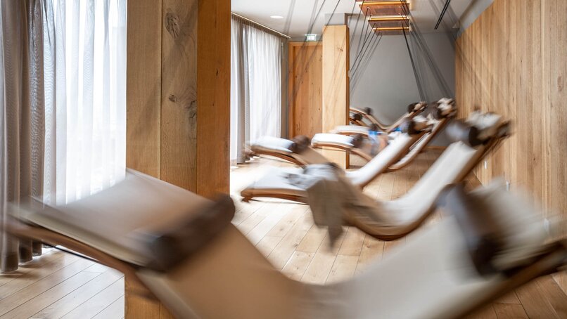 Bewegende Schwebeliegen mit einem weißen Polster in einem Raum mit Holzoptik und großer Fensterfront | © Silvretta Montafon - blateral