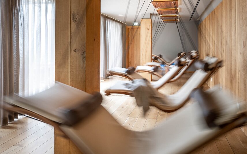 Bewegende Schwebeliegen mit einem weißen Polster in einem Raum mit Holzoptik und großer Fensterfront | © Silvretta Montafon - blateral
