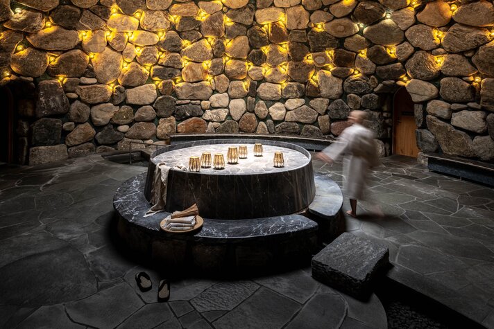 Eine Frau läuft durch das Tepidarium, welches in goldenes Licht getaucht ist mit einem Loch in der Decke. | © Silvretta Montafon - blateral