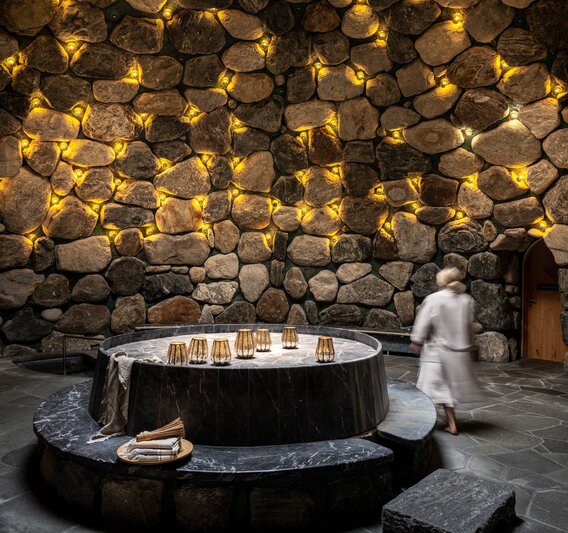 Eine Frau läuft durch das Tepidarium, welches in goldenes Licht getaucht ist mit einem Loch in der Decke.  | © Silvretta Montafon - blateral