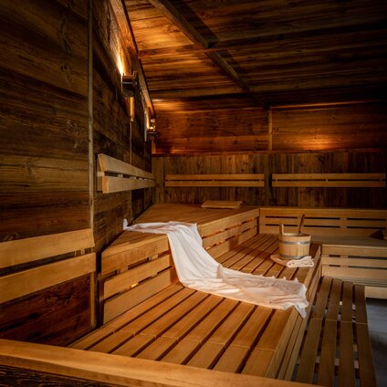Finnische Sauna mit Holzwänden und Holzbänken auf denen ein Handtuch und eine Wasserschale aus Holz stehen | © Silvretta Montafon - blateral