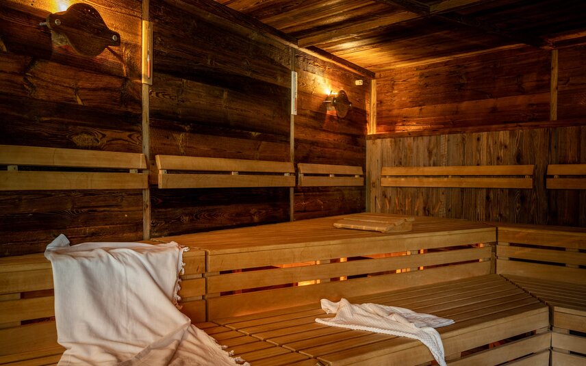 Eine finnische Sauna mit Holzwänden und Holzbänken, auf welchem ein weißes Handtuch liegt und ein Wasserkübel aus Holz steht | © Silvretta Montafon - blateral
