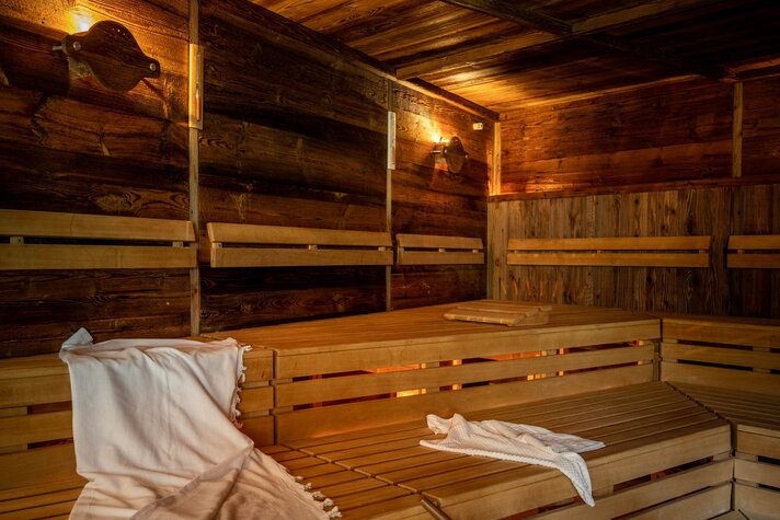 Eine finnische Sauna mit Holzwänden und Holzbänken, auf welchem ein weißes Handtuch liegt und ein Wasserkübel aus Holz steht | © Silvretta Montafon - blateral