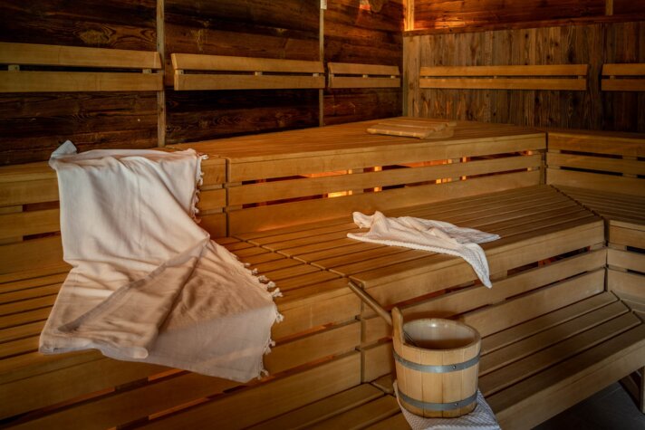Gold Spa im Sporthotel Silvretta Montafon | © Silvretta Montafon - blateral Eine finnische Sauna mit Holzwänden und Holzbänken, auf welchem ein weißes Handtuch liegt und ein Wasserkübel aus Holz steht | © Silvretta Montafon - blateral