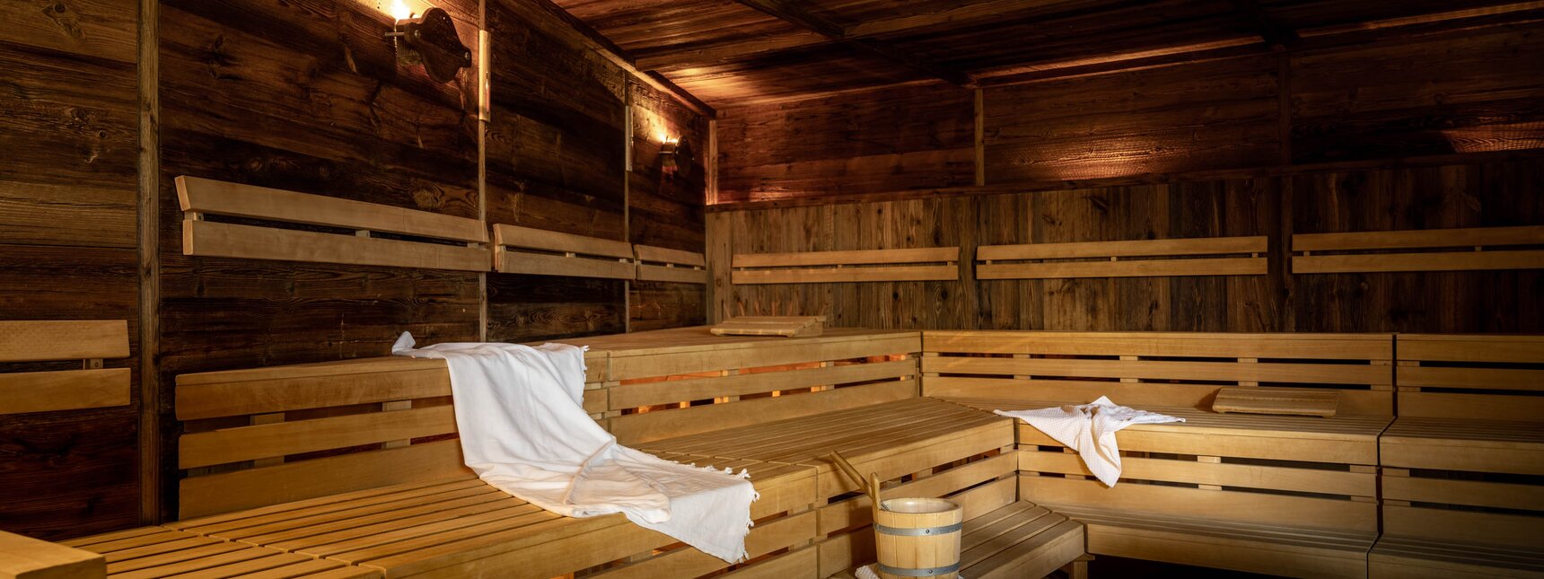 Eine finnische Sauna komplett in Holz mit Sitzbänken und einem weißen Handtuch | © Silvretta Montafon - blateral