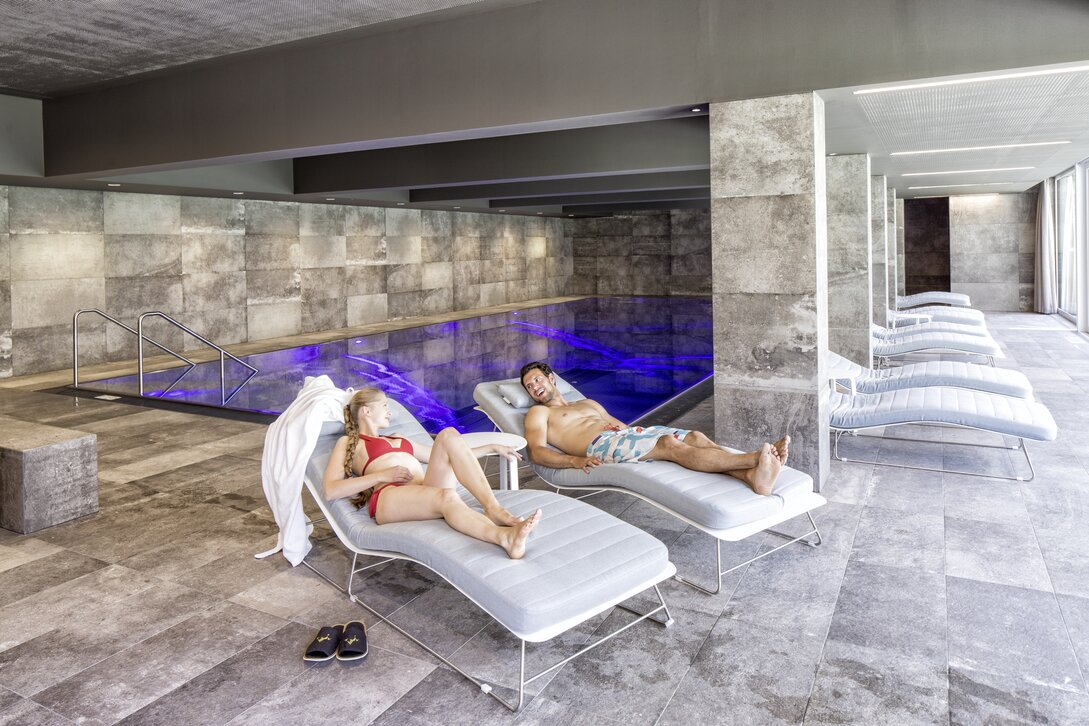 Ein Paar genießt die Zweisamkeit auf den Liegen vor dem Kristallpool im Sporthotel Silvretta Montafon | © Silvretta Montafon - Markus Gmeiner