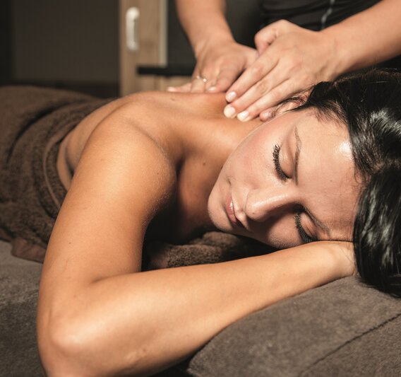 Eine dunkelhaarige Frau liegt auf einer Massageliege und bekommt eine Rückenmassage | © Silvretta Montafon
